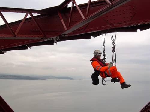 Image of maintenance worker from Amey suspended on ropes from the Forth Bridge over the River Forth